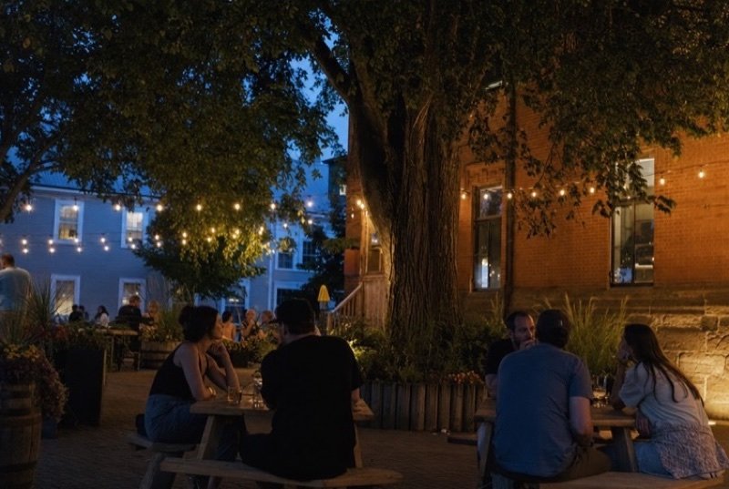 String lights over picnic tables on a brewery patio by a red-brick building at dusk, the kind of local spot SEO Brantford helps diners find
