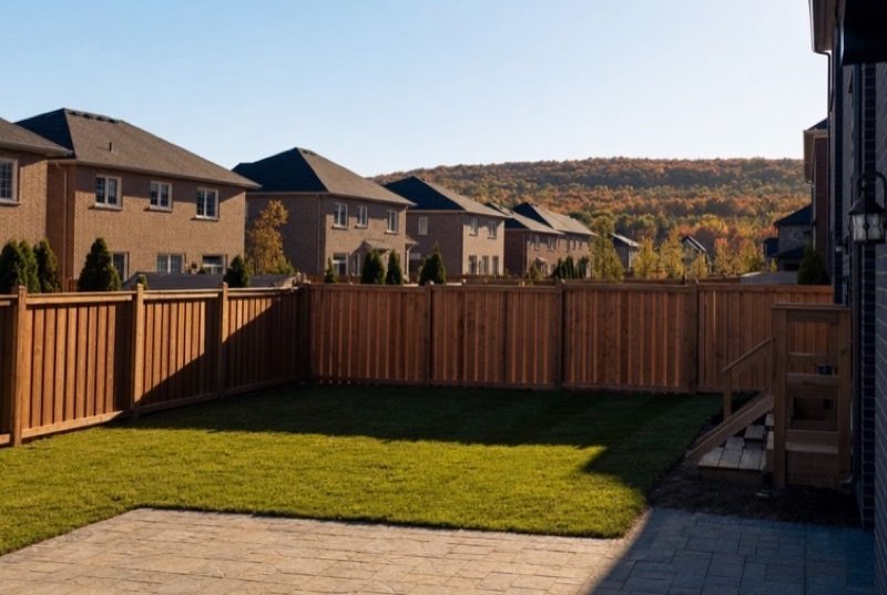 A newly finished backyard with fresh sod, a stamped-concrete patio and a wooden privacy fence, brick houses next door